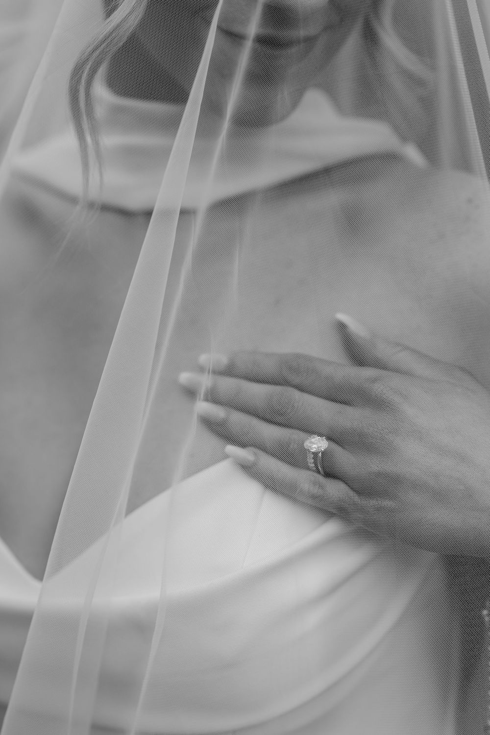 Black and white photo of a bride in a silk gown and veil, showcasing her elegant diamond engagement ring.
