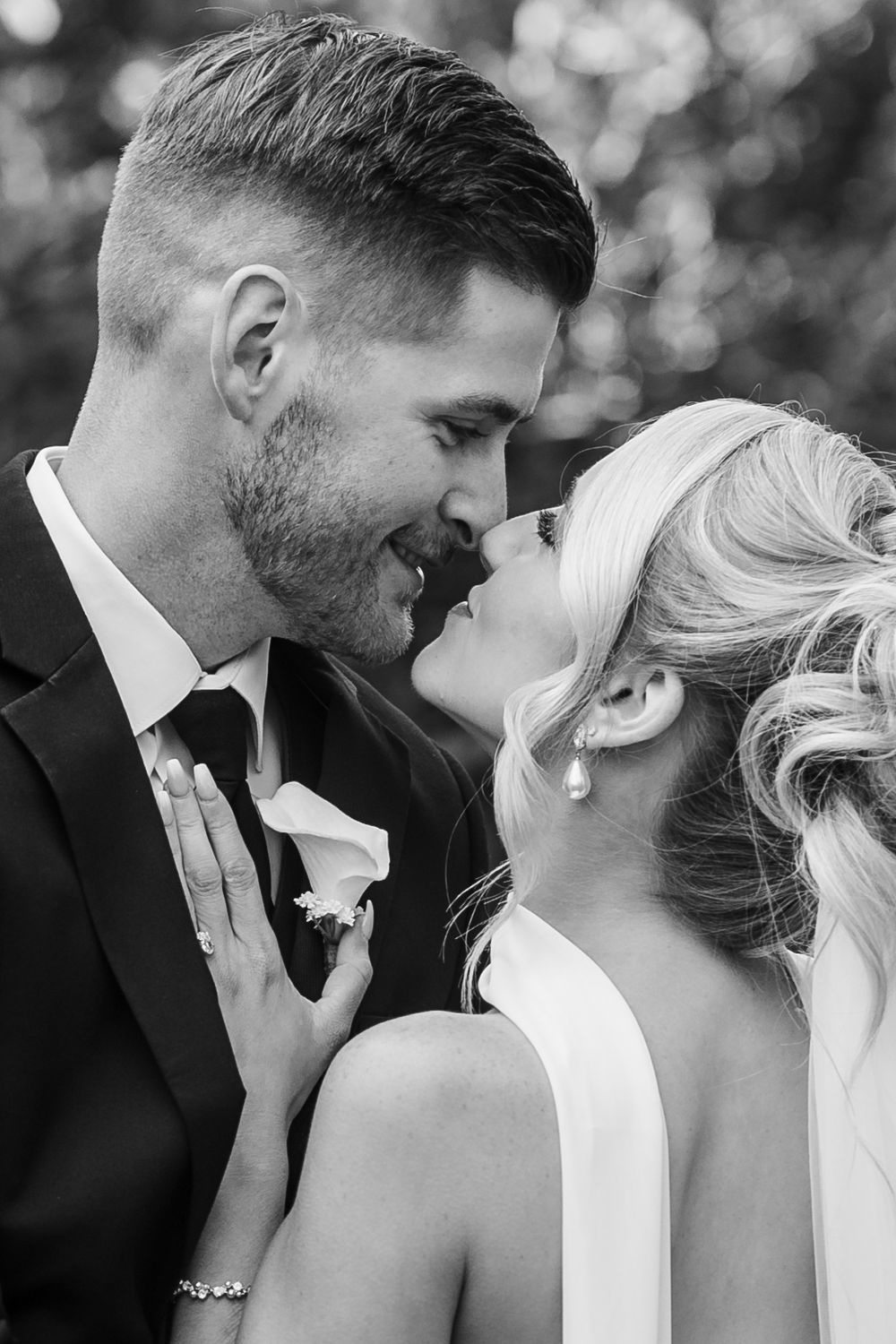 Black and white wedding photo of bride and groom sharing an intimate moment, almost kissing, in formal attire.