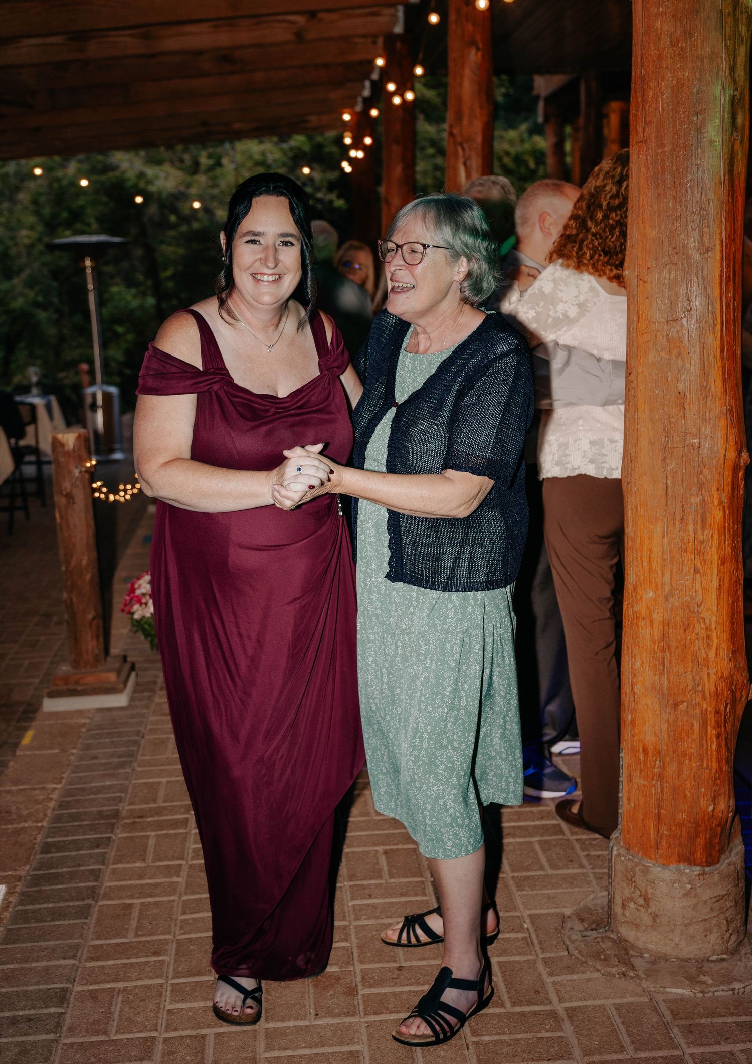 Two women dancing together at an outdoor wedding reception under string lights.