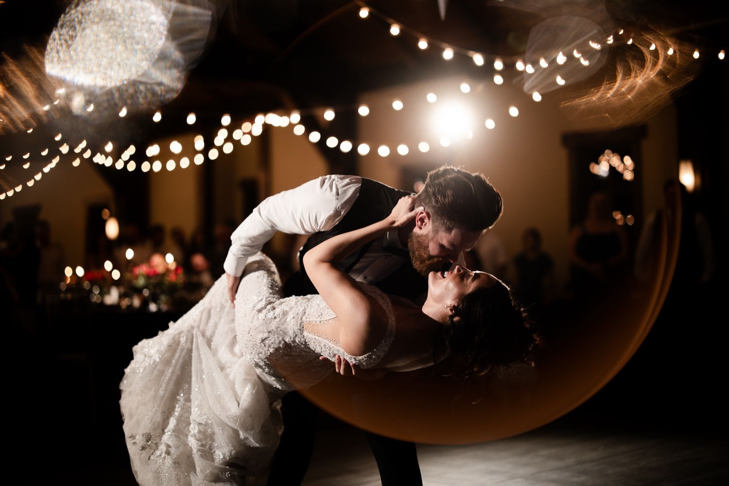 Bride and groom share a romantic dip dance under warm string lights at their wedding reception.