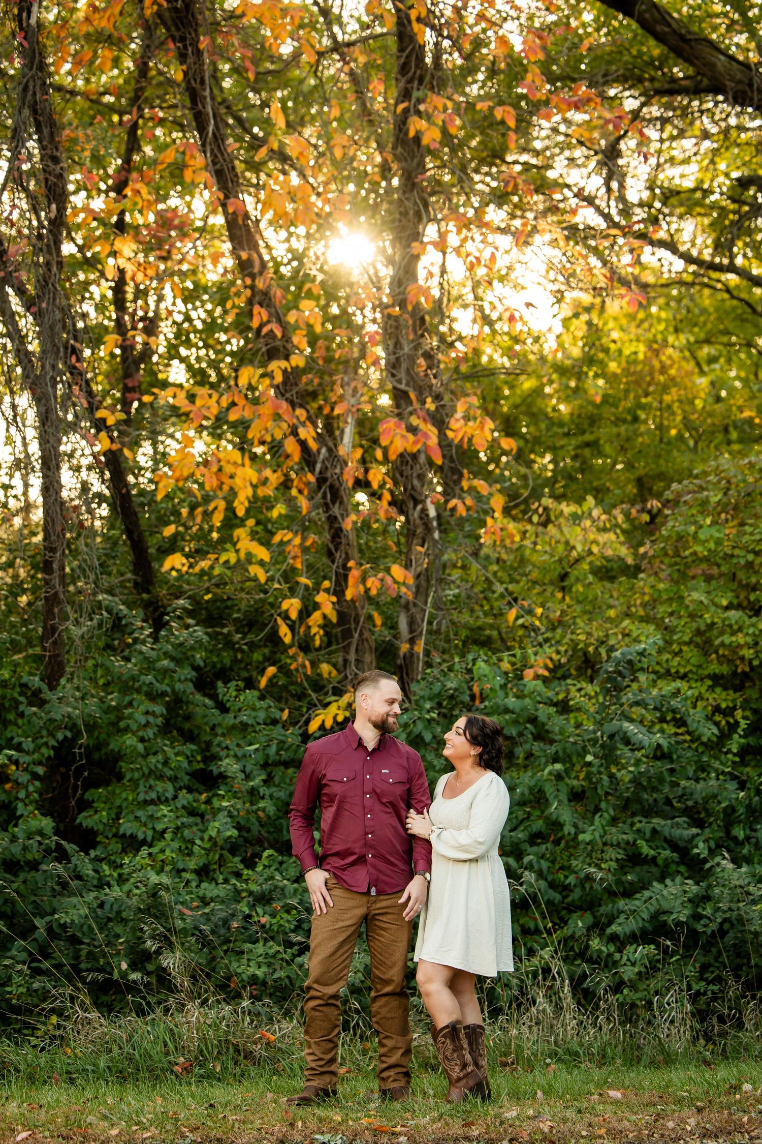 Couple sharing a romantic moment in autumn forest with golden sunlight filtering through colorful fall foliage.