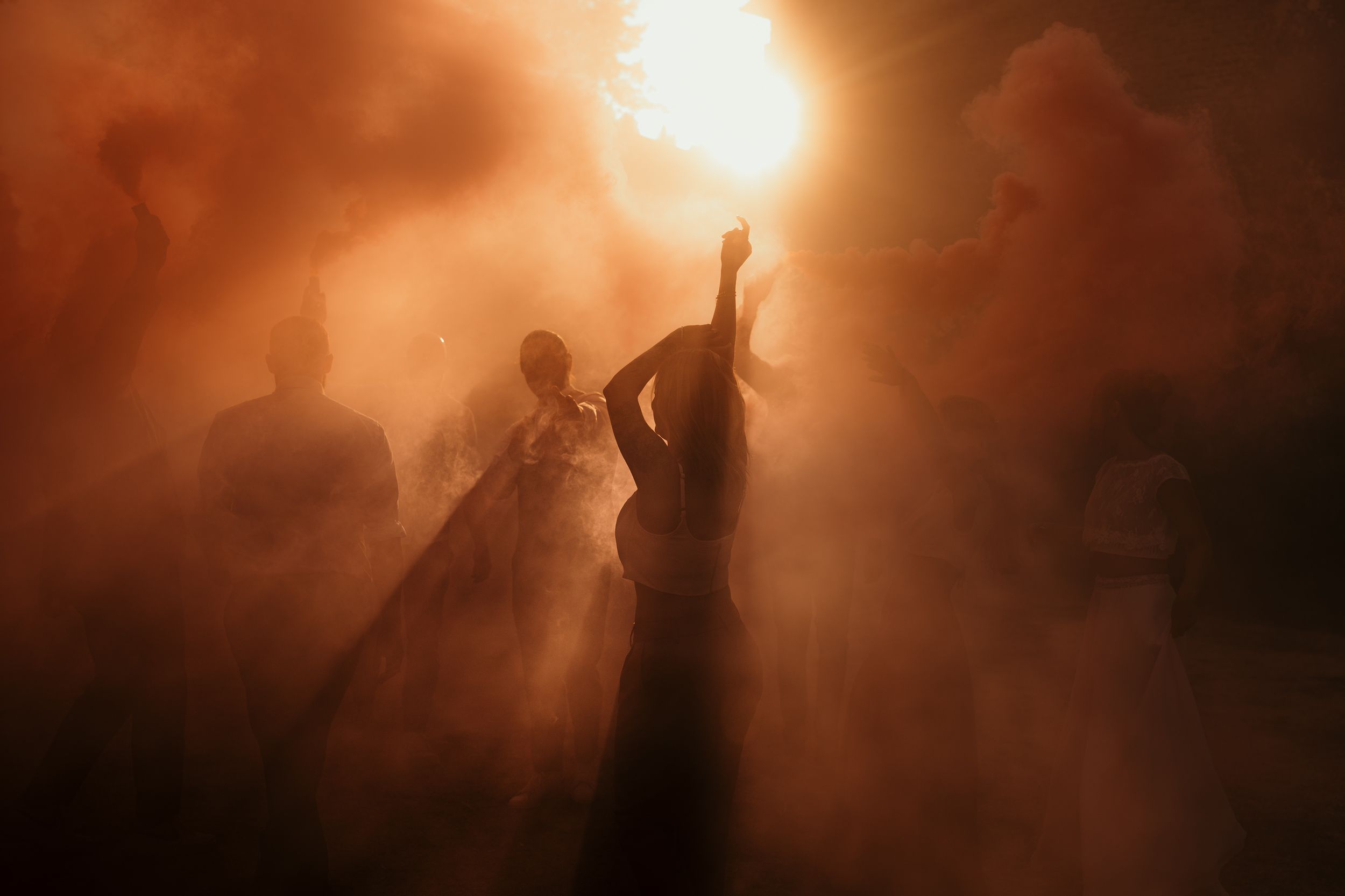 Silhouettes of dancing people against a dramatic orange-lit foggy background.