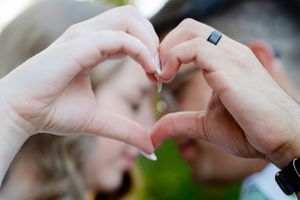 Two hands forming a heart shape gesture together against a blurred background.