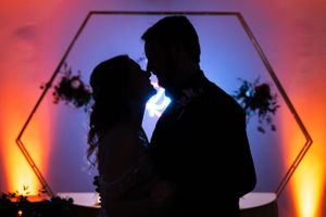 Silhouetted couple embraces in front of illuminated hexagonal frame with orange and blue ambient lighting.