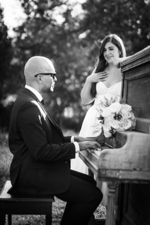 A black and white wedding photo of a couple with a piano outdoors, featuring a beautiful bouquet of flowers.