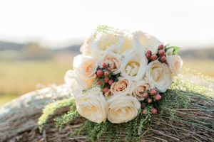Beautiful bouquet of cream roses and burgundy berries resting on rustic wood in golden sunlight.