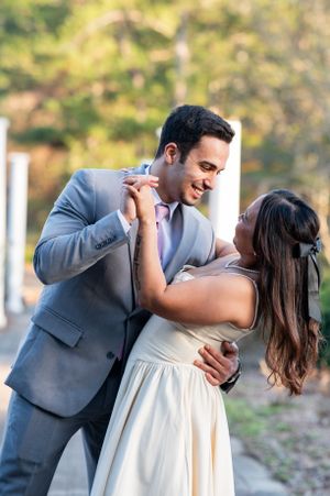 A romantic couple in wedding attire share a tender dip dance pose outdoors with natural lighting and greenery in background.