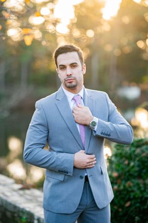 Professional portrait of person in light gray suit and pink tie against blurred golden sunset background.