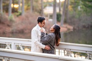 A couple shares a romantic moment while standing on a white bridge over a lake during golden hour.