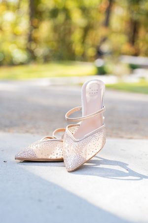 Elegant blush pink crystal-embellished pointed toe mule slippers sit in natural sunlight on concrete surface.