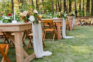 Rustic outdoor wedding reception setup with wooden tables decorated with floral arrangements and white runners.
