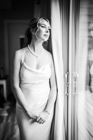 Black and white portrait series showing a person in a white dress looking pensively through a window.