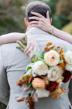 Close up of a couple embracing with a peach and white floral bouquet visible from behind.