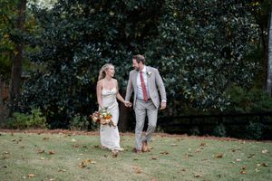 A couple walks hand in hand through a garden setting with fall leaves on the ground.