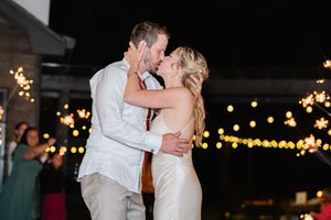 A couple shares a romantic kiss on the dance floor at a wedding reception with twinkling lights in the background.