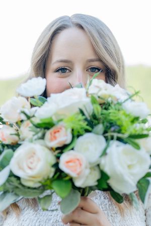 A beautiful bouquet of white and peach roses with green foliage held up close to the camera in soft natural light.