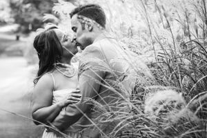 A romantic black and white outdoor photo showing a couple embracing amid tall grasses and sunlight.