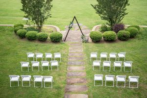 White garden chairs arranged symmetrically on a lush green lawn with a stone pathway and manicured shrubs.