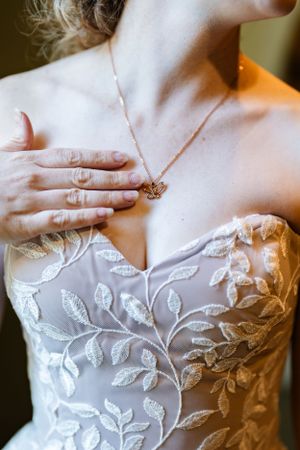 Close-up of delicate floral lace wedding dress bodice with sheer neckline and dainty necklace.