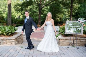 A couple in formal wedding attire dancing outdoors on a stone patio surrounded by lush greenery.