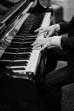 Black and white close-up of hands playing a grand piano keyboard showing elegant finger placement.