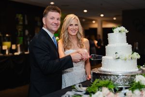A wedding couple cuts their elegant white tiered cake decorated with fresh flowers at their reception celebration.