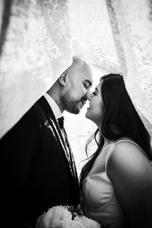 A romantic black and white wedding portrait captures an intimate moment between newlyweds against a soft background.