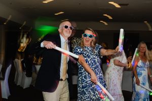 People dancing and socializing at an indoor party or celebration event with green lighting visible in the background.