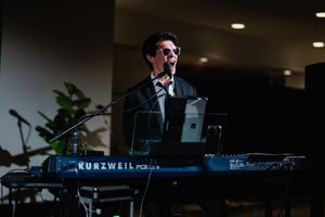 Musician performs on a Kurzweil keyboard during a live performance in a dimly lit venue.