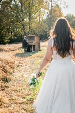 An outdoor wedding scene with a white dress and pianist at an upright piano in a sunlit autumn field.