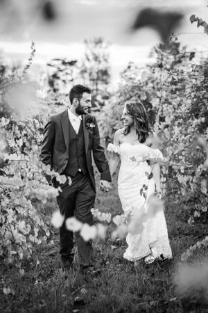 A couple walking hand in hand through a garden on their wedding day, captured in black and white photography.