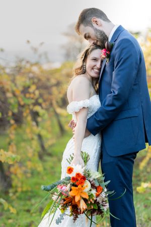 A wedding couple shares an intimate moment outdoors with a vibrant fall bouquet of orange and red flowers.