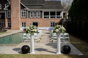 Outdoor wedding ceremony setup with white chairs arranged in rows on a brick courtyard surrounded by buildings.