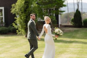A couple walks hand in hand through a sunlit garden on their wedding day, with the bride wearing a flowing white dress.