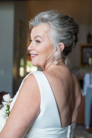 Woman in white sleeveless dress smiling and looking to the side with silver hair styled up in an elegant updo.