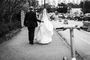 A bride and groom walk down a sidewalk together on their wedding day, captured in black and white.