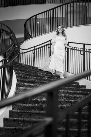 A bride in a white lace dress poses elegantly on curved stone steps with black railings in a black and white photo.