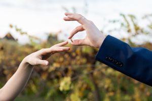 Two hands reaching towards each other with an outdoor nature scene in the blurred background.