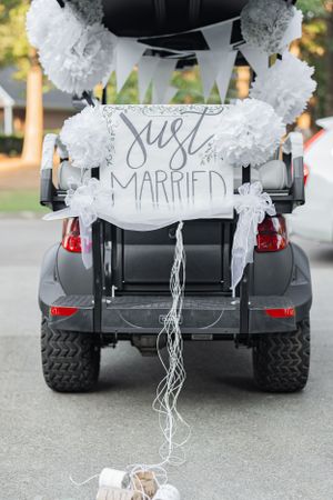 Decorated wedding golf cart with 'Just Married' sign and white pom pom decorations on the back.