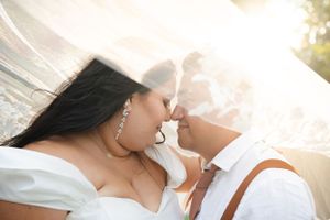 Romantic wedding couple shares an intimate moment under a flowing veil during sunset.