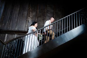 A couple walking down a dark wooden staircase during their rustic barn wedding celebration.