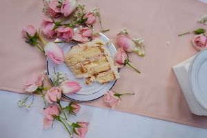 A slice of layered cake garnished with delicate pink roses on a white plate against a pink tablecloth.