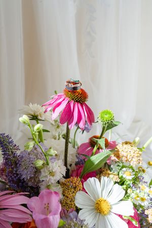 Wedding rings resting on a pink echinacea flower surrounded by a colorful wildflower bouquet.