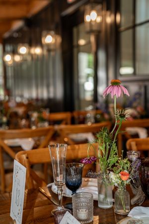Elegant rustic wedding reception table with wildflower centerpieces, mixed glassware, and warm string lights overhead.