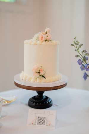 Elegant single-tier white wedding cake with pink roses on a wooden cake stand.
