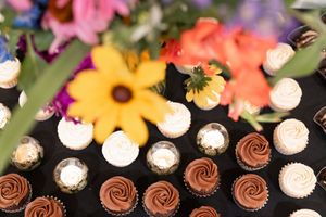 Assortment of chocolate and vanilla frosted cupcakes displayed with vibrant colorful flowers at a wedding reception.