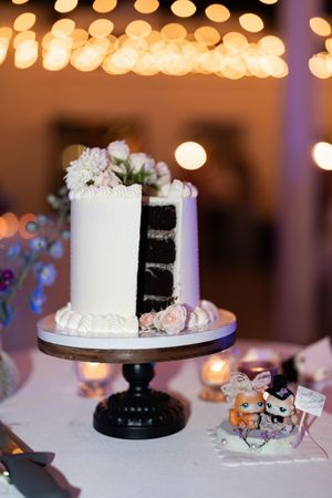 Cut white wedding cake revealing dark chocolate layers on a wooden stand with bokeh lights.