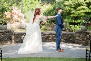 Bride in white off-shoulder gown and groom in navy suit share a first look in a lush garden.
