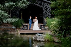 Bride and groom exchange vows on a wooden dock beside a tranquil pond in a lush green garden.