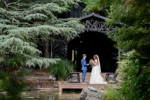 Bride and groom exchange vows on wooden dock surrounded by lush trees and tranquil pond.
